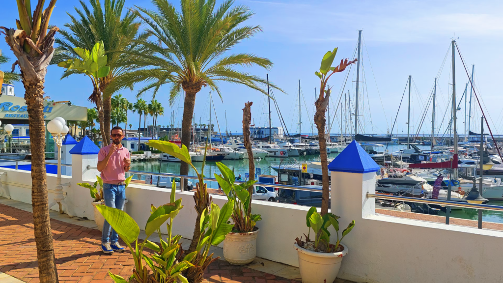 Izidor Isakov beside palm trees overlooking sailboats in Estepona Marina.