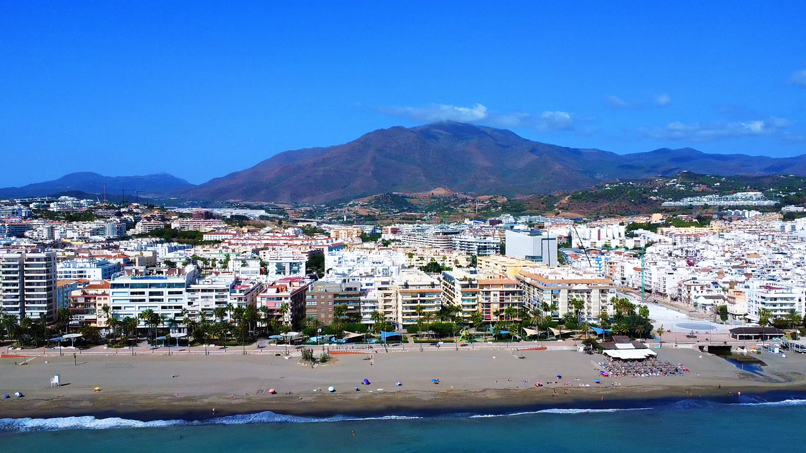 Aerial view of La Rada beach, Estepona’s seafront apartments and promenade, with Sierra Bermeja mountains behind the town.
