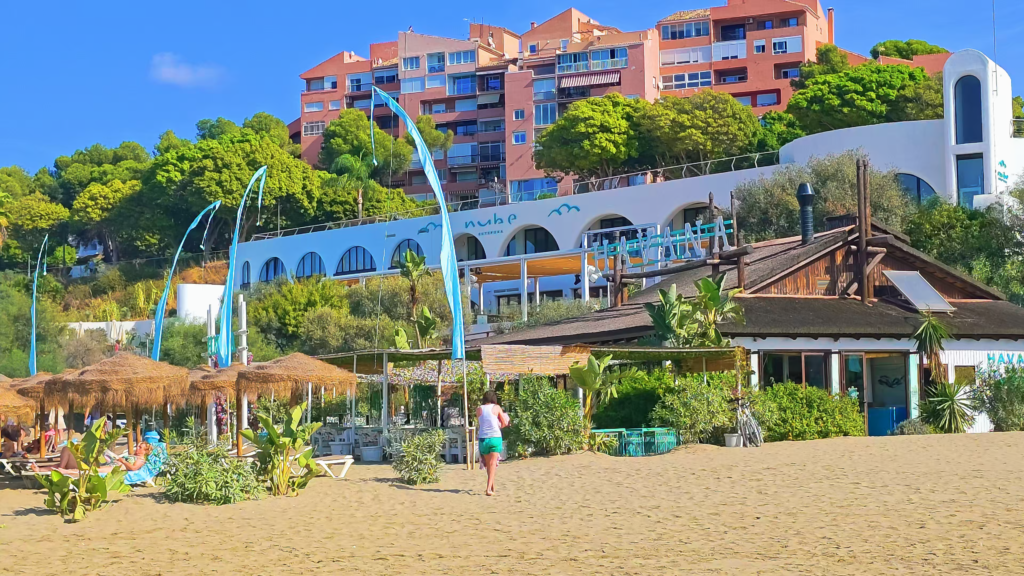 Beach restaurant beneath hillside apartment buildings beside a sandy beach in Estepona.