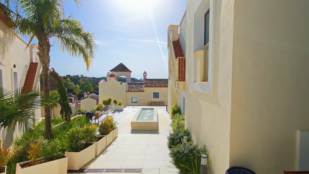 Landscaped courtyard with palm trees and a long water feature between cream-coloured buildings in Estepona.